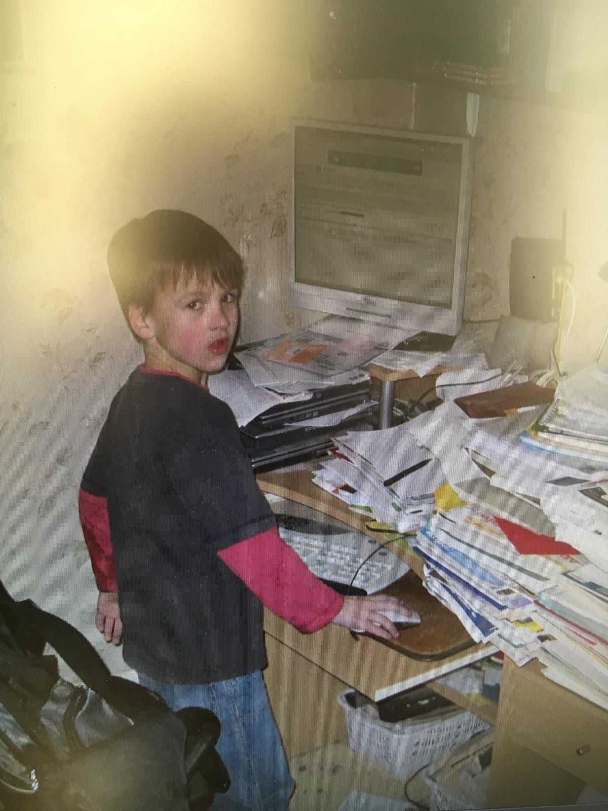 Old photo from 2010 of the author of the site pictured as a child browsing the computer with a messy desk.
